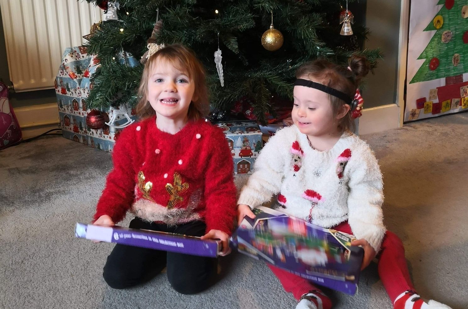 Two children sitting in front of christmas tree with gifts